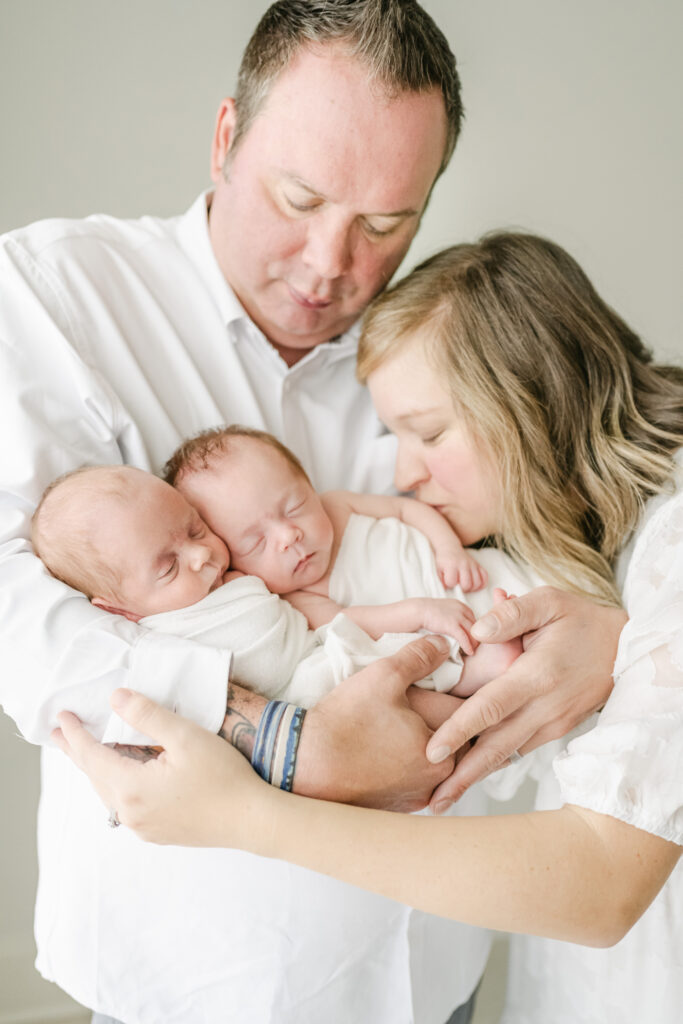 Dad holding twin babies with mom kissing in newborn session in atlanta studio.