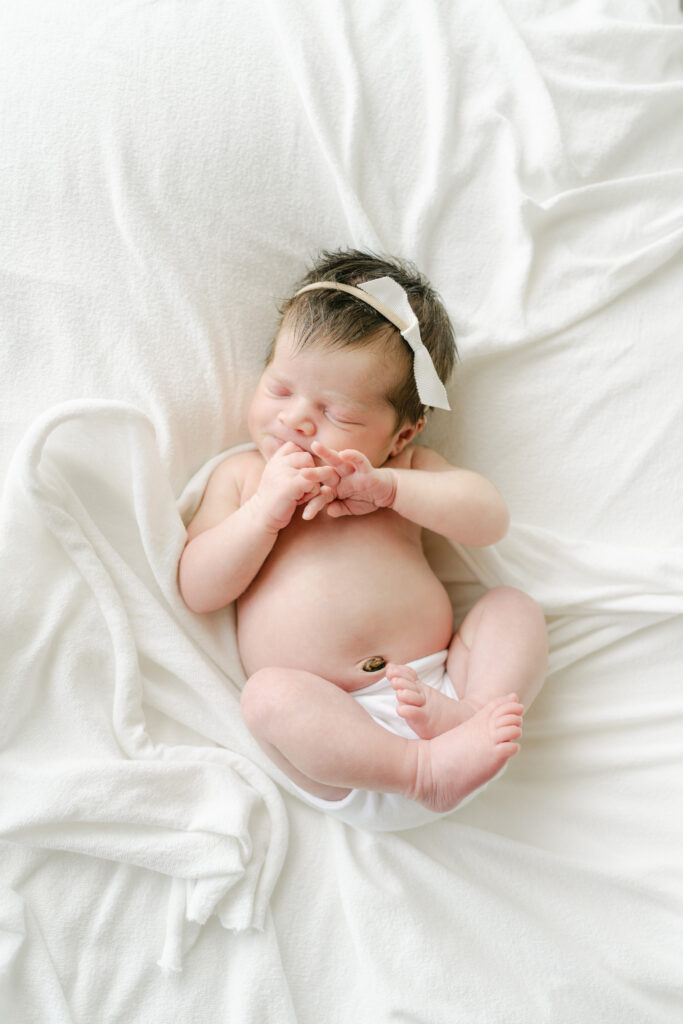 Newborn baby girl on all white newborn stretch.